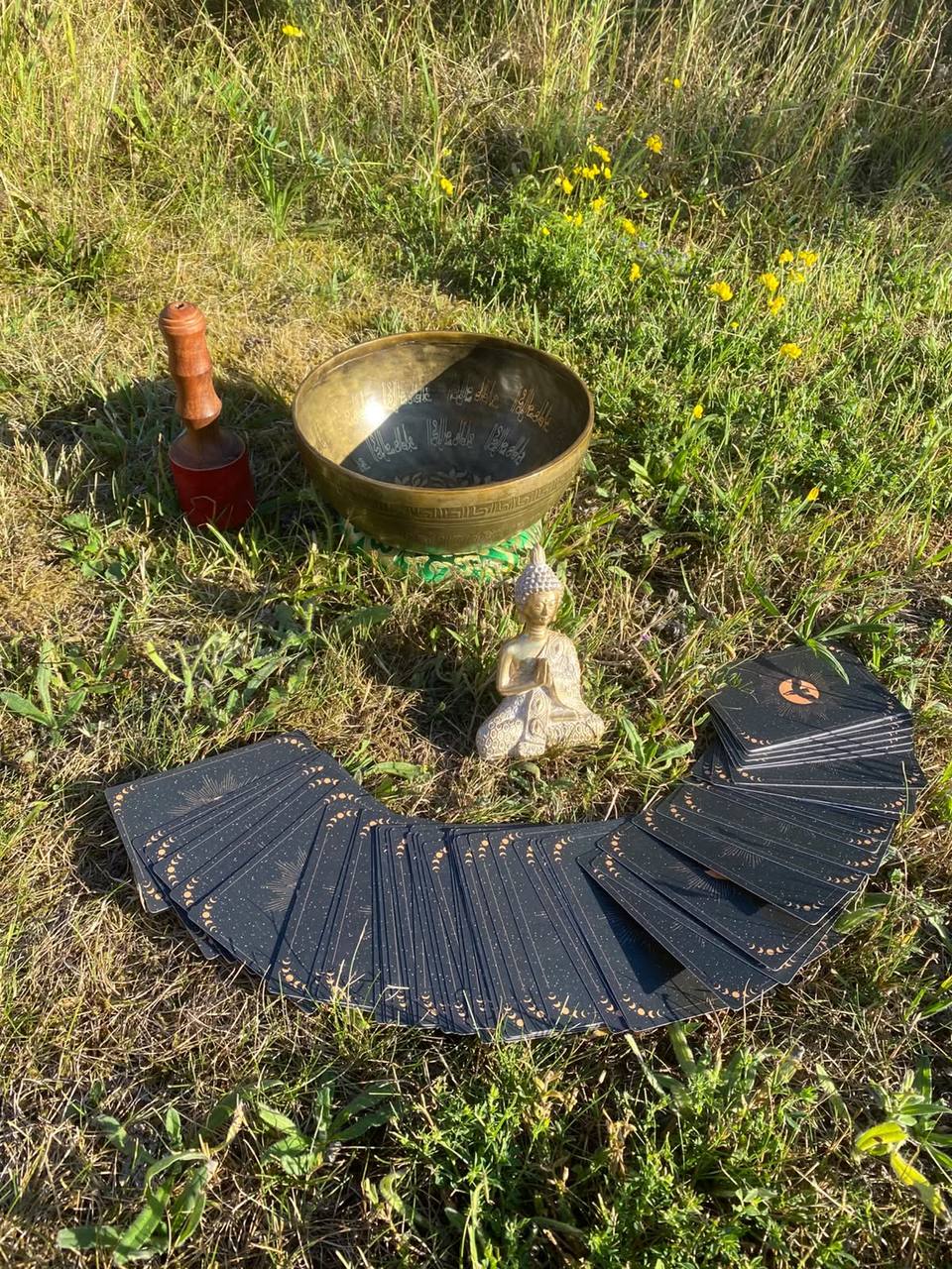 Klangschale, Buddha-Figur und aufgefächerte Karten auf einer Sommerwiese