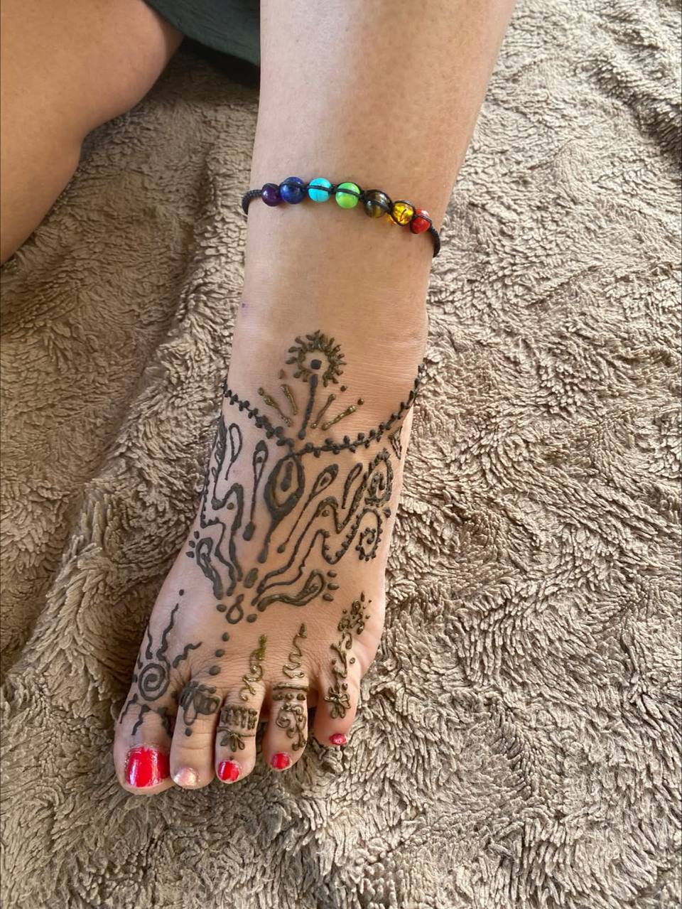 Fuß mit geschwungenen Henna-Ornamenten und Chakra-Fußkettchen